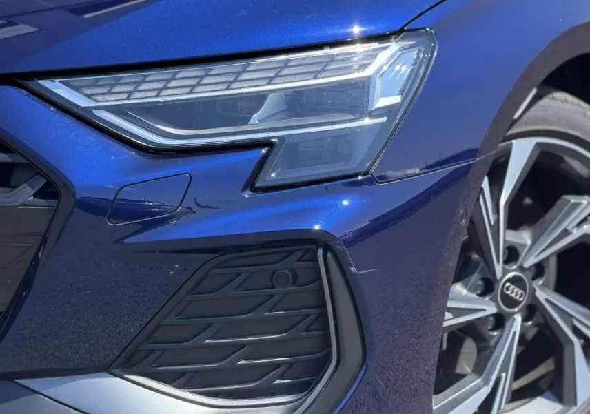 Gros plan sur l'avant droit bleu Navarre de l'Audi A3 Sportback 2025, mettant en valeur le phare Matrix LED et la jante alliage.