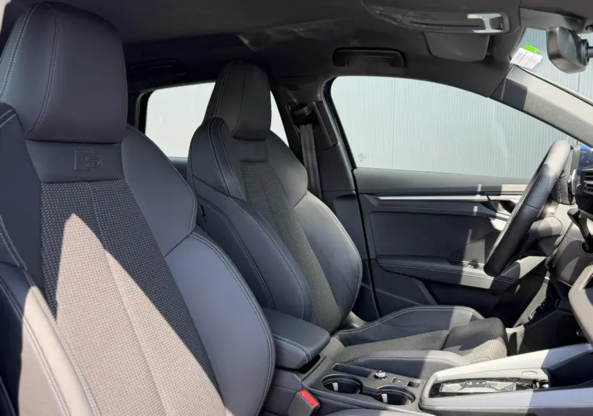 Vue intérieure côté droit des sièges sport noirs avec surpiqûres blanches et volant cuir de l'Audi A3 Sportback S-Line 2025.
