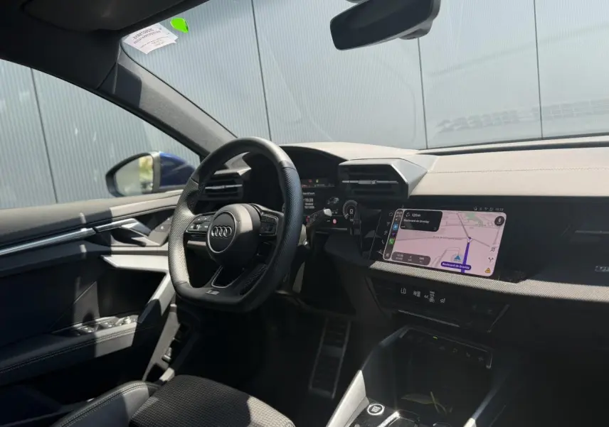 Vue intérieure côté conducteur de l'Audi A3 Sportback bleu Navarre, avec tableau de bord numérique et écran central tactile.