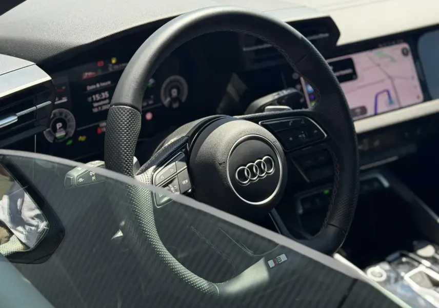 Vue rapprochée du volant cuir perforé avec logo Audi et tableau de bord numérique de l’A3 Sportback 2025.