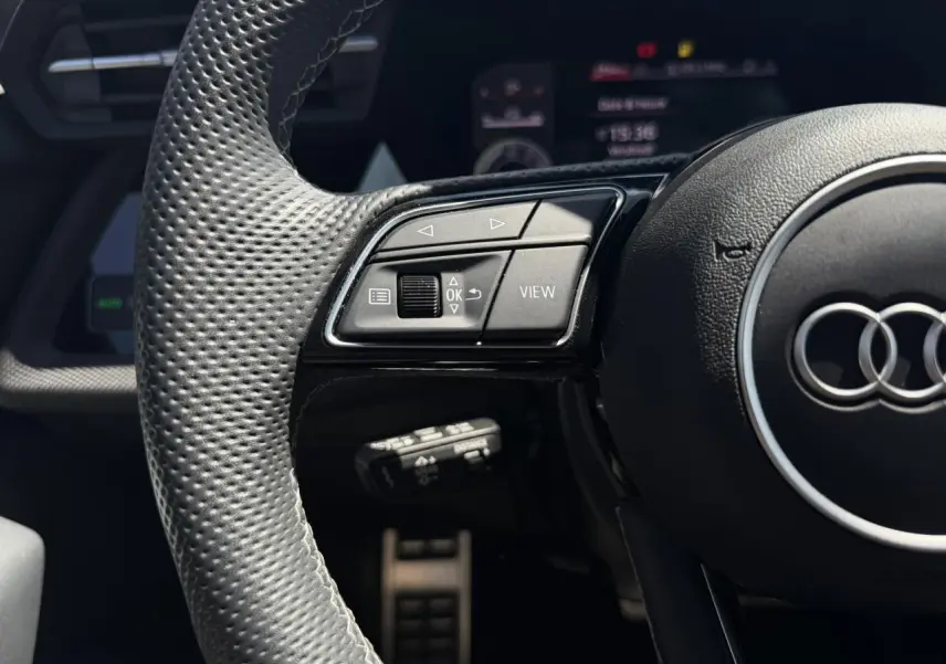 Gros plan sur le volant cuir perforé de l'Audi A3 Sportback 2025 avec commandes multifonctions côté gauche.