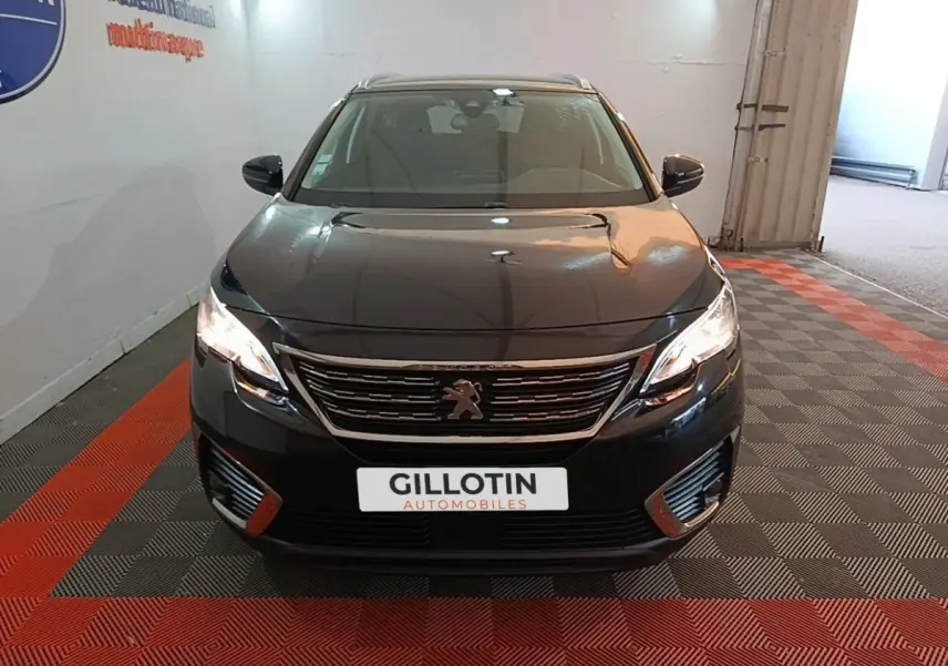 Peugeot 5008 noir vue de face, phares allumés, calandre chromée et logo lion visible, intérieur clair.