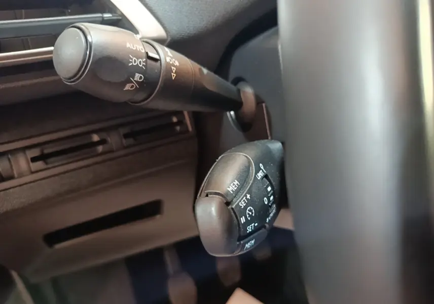 Gros plan sur les commandes au volant du Peugeot 5008 noir, mettant en valeur les boutons de régulateur de vitesse et d'éclairage.