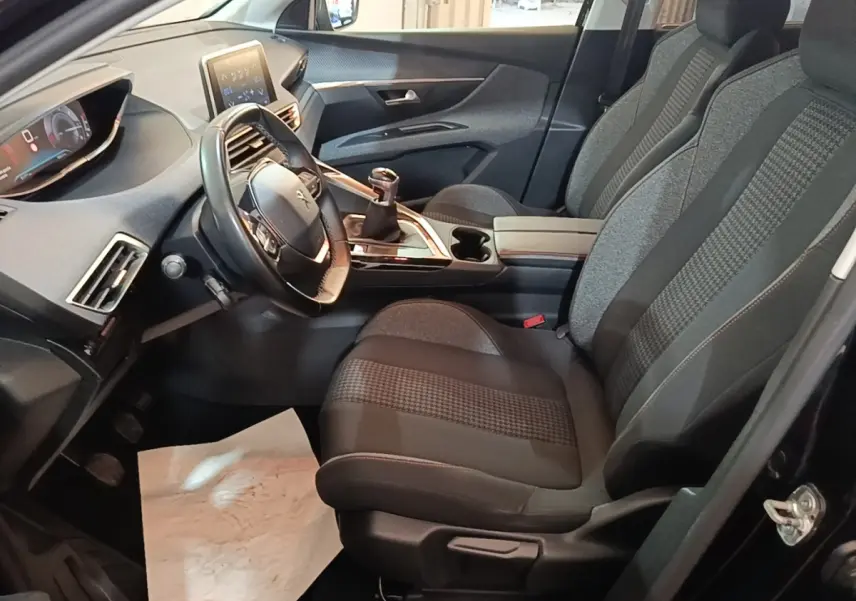 Intérieur avant droit du Peugeot 5008 noir, montrant sièges tissu, volant cuir multifonctions et tableau de bord digital.