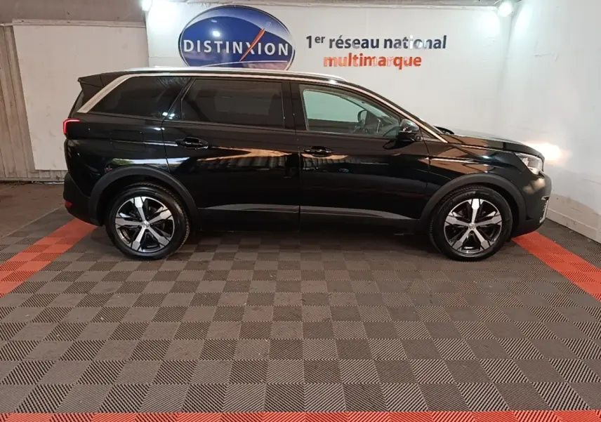 Peugeot 5008 noir vue de profil côté gauche dans un showroom avec jantes alliage et vitres teintées.
