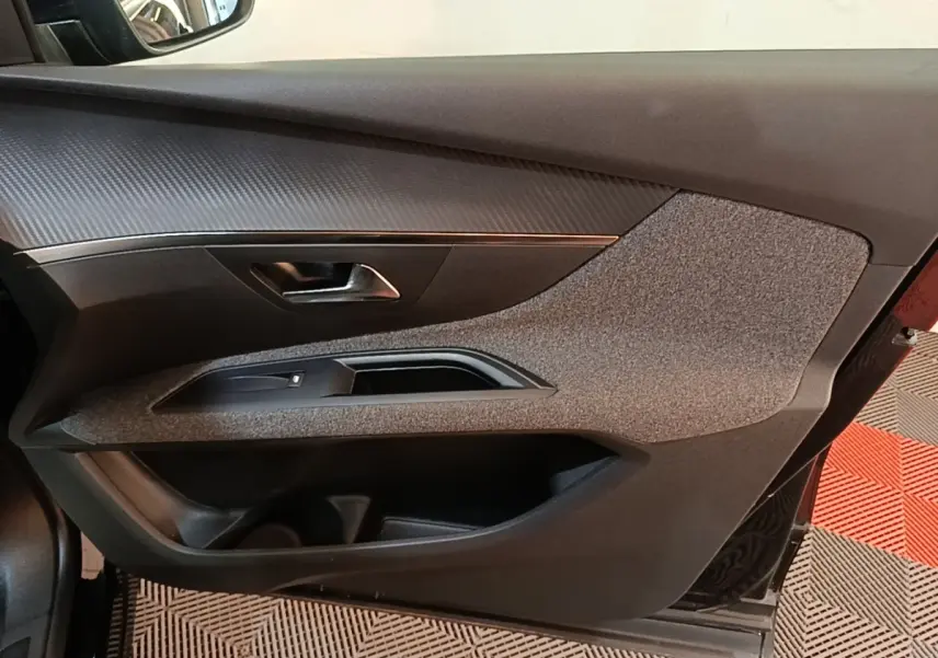 Vue intérieure côté gauche de la porte avant d’un Peugeot 5008 noir avec garniture tissu et plastique noir.