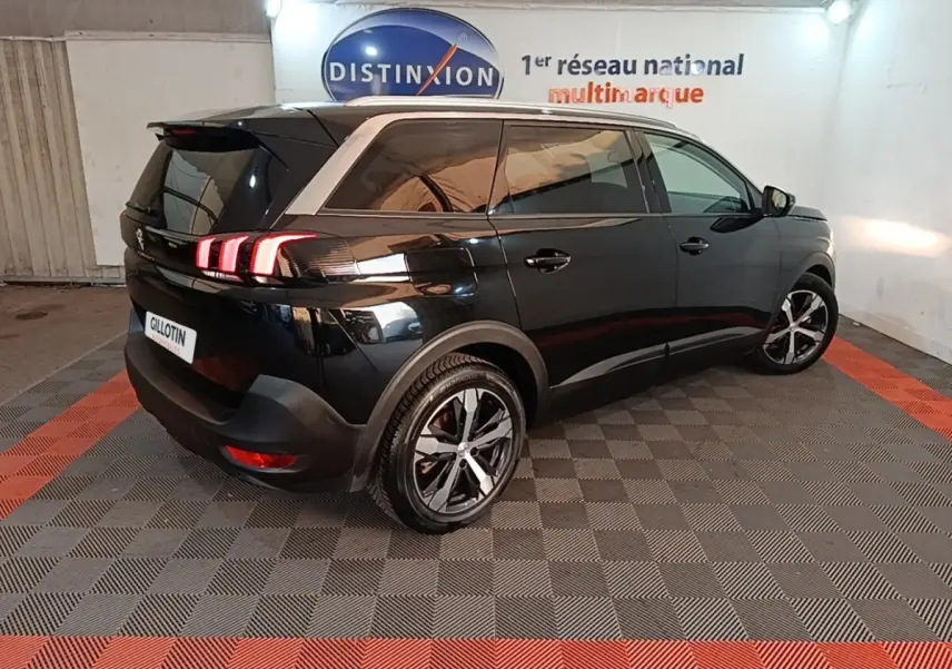 Peugeot 5008 noir vue 3/4 arrière droit en intérieur, feux arrière allumés et jantes alliage bicolores.