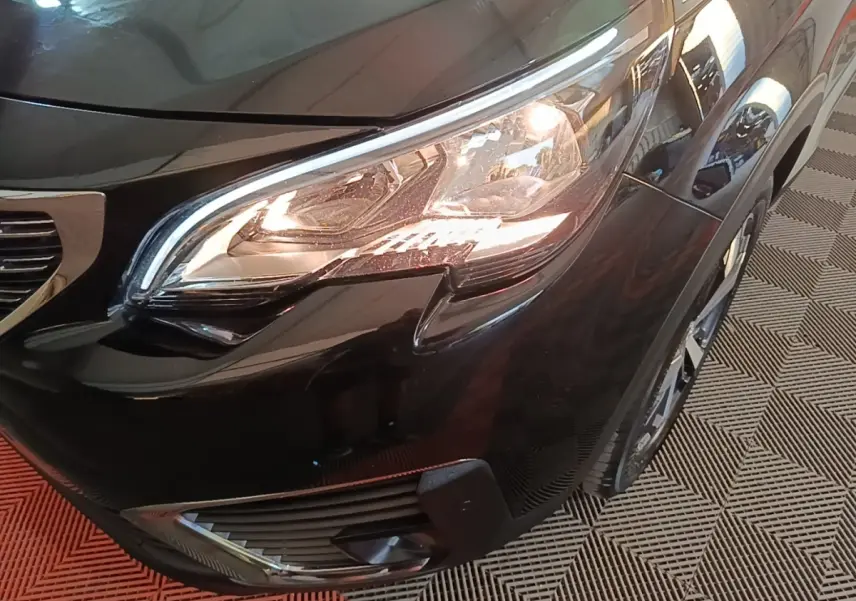 Gros plan sur le phare avant droit d’un Peugeot 5008 noir, avec partie de la calandre et roue visible.