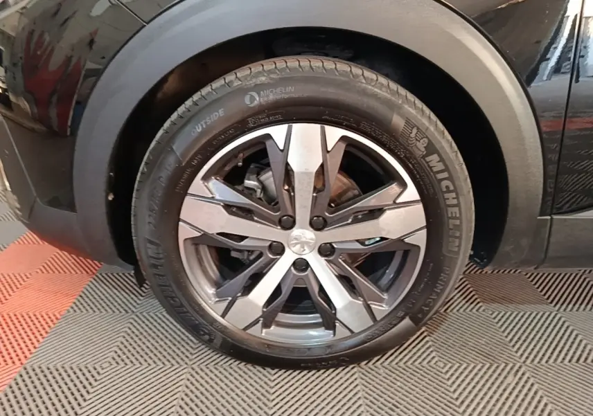 Gros plan sur la roue avant gauche noire d’un Peugeot 5008 avec jante alliage et pneu Michelin.