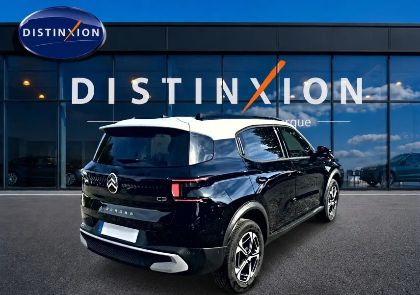 Vue 3/4 arrière droite d'une Citroën C3 Aircross noire avec toit blanc, garée devant une vitrine Distinxion.