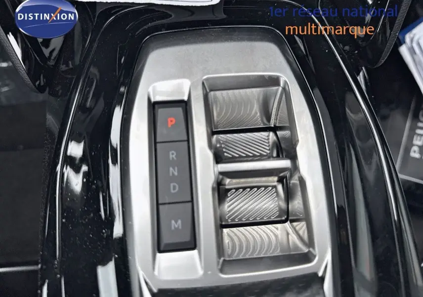 Gros plan sur la console centrale noire métallisée du Peugeot 2008 Hybrid avec sélecteur de boîte automatique et boutons de vitesses.