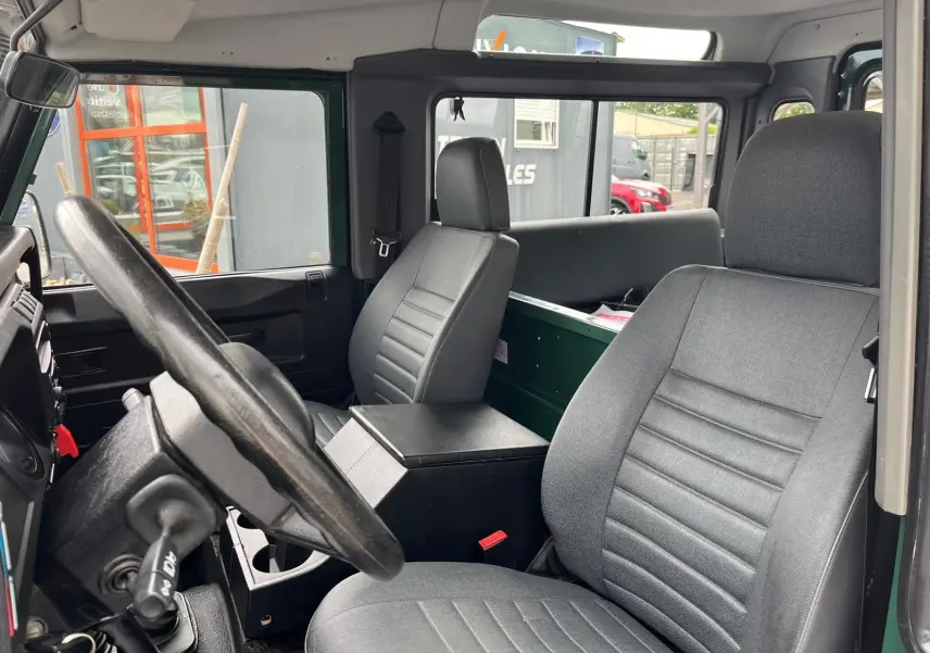 Intérieur du Land Rover Defender 90 Hard Top vert, vue côté conducteur avec sièges gris et tableau de bord simple.