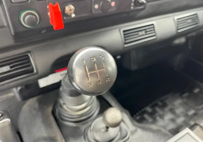 Gros plan sur le levier de vitesses manuel du Land Rover Defender 90 Hard Top vert de 2004, intérieur simple et fonctionnel.