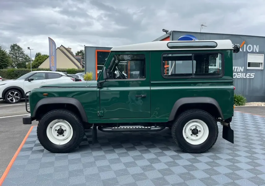 Profil côté gauche d'un Land Rover Defender 90 Hard Top vert avec toit blanc, marchepieds et roues blanches visibles.