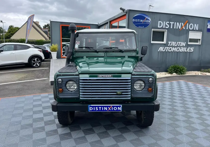 Vue frontale d'un Land Rover Defender 90 vert avec snorkel et marchepieds, stationné devant un concessionnaire.