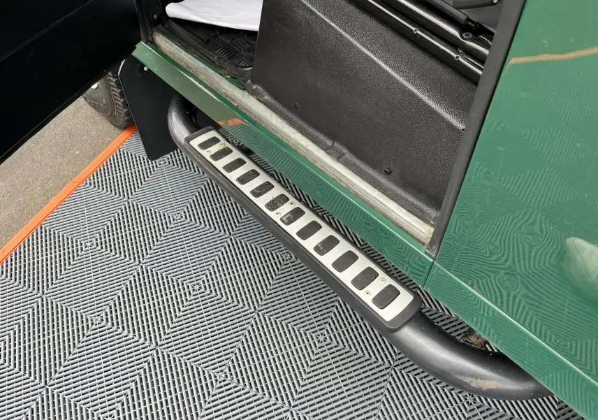 Gros plan sur le marchepied latéral droit vert d’un Land Rover Defender 90 Hard Top 2004 avec porte ouverte.