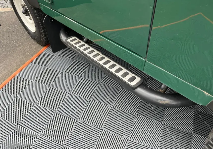 Vue rapprochée du marchepied côté gauche d’un Land Rover Defender 90 vert 2004 Hard Top avec pneus tout-terrain.
