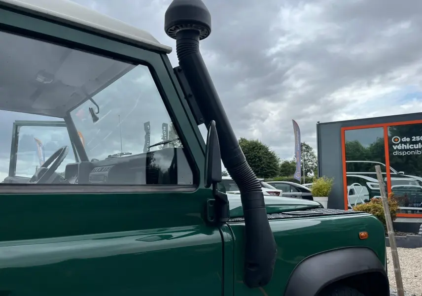 Vue latérale gauche rapprochée d'un Land Rover Defender 90 vert avec snorkel et toit dur blanc visible.