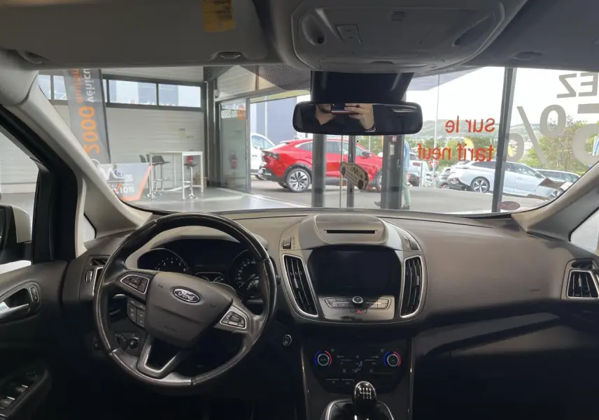 Vue intérieure frontale du tableau de bord et volant cuir noir de la Ford C-MAX blanc, avec écran tactile éteint.