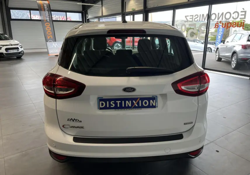 Vue arrière d'un Ford C-MAX blanc 2018 en showroom avec feux arrière rouges et vitre arrière teintée.