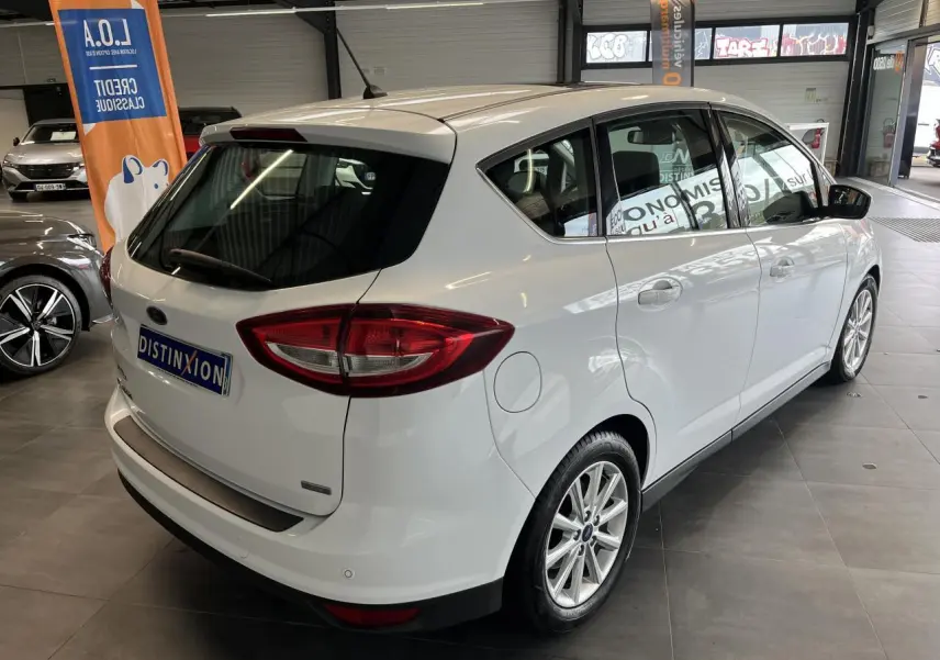 Vue 3/4 arrière droite d'un Ford C-MAX blanc en showroom avec jantes alliage et vitres teintées.