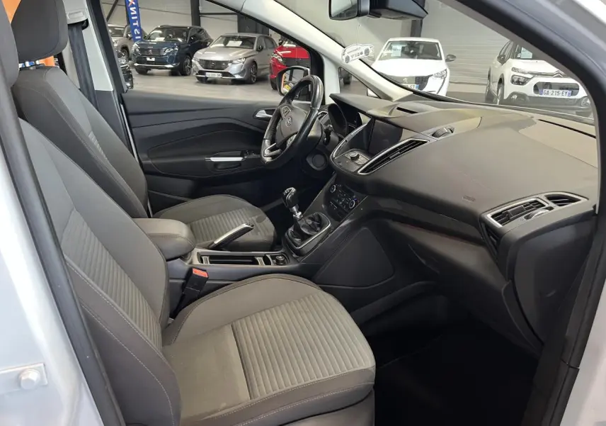 Intérieur avant droit du Ford C-MAX blanc 2018, montrant sièges tissu gris, volant cuir et console centrale avec écran tactile.