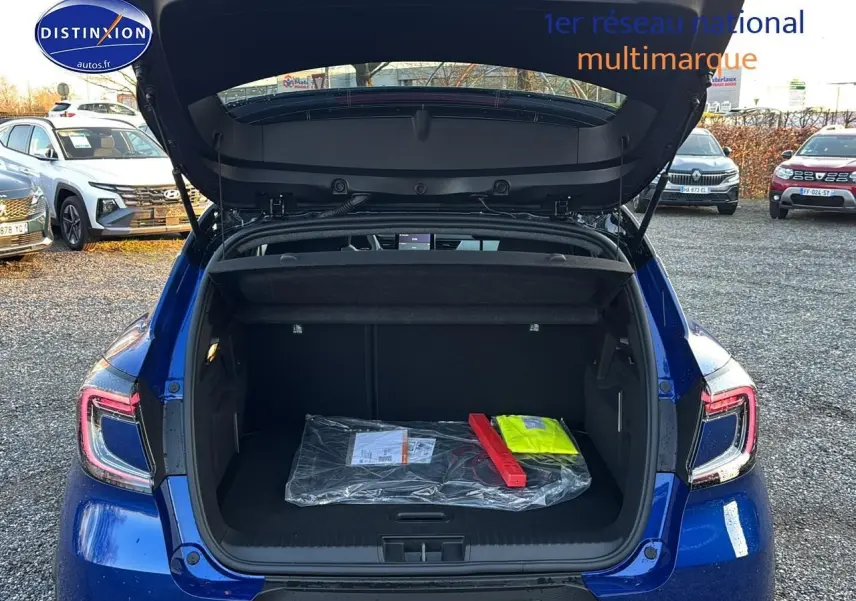 Vue arrière d’un Renault Captur bleu iron avec coffre ouvert montrant un triangle de signalisation et un gilet jaune à l’intérieur.