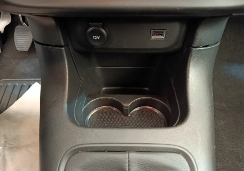 Gros plan de la console centrale noire avec prise 12V, port USB et porte-gobelets dans une Citroën C3 blanche.