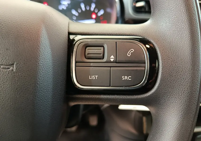 Gros plan sur les commandes multifonctions noires du volant de la Citroën C3 blanche, côté gauche.