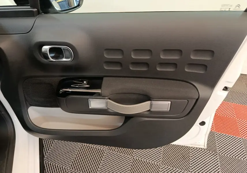 Vue intérieure du panneau de porte avant gauche de la Citroën C3 blanche, avec poignée en cuir et commandes électriques.