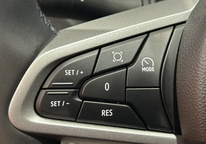 Détail des commandes au volant côté gauche du Dacia Bigster 2026, boutons noirs avec marquages blancs sur fond argenté.