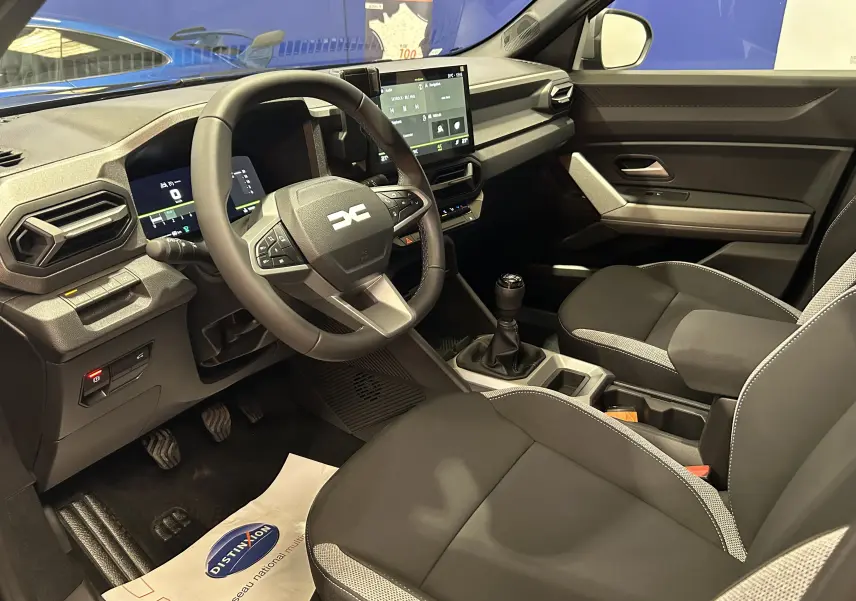 Vue intérieure côté conducteur du Dacia Bigster 2026 avec volant multifonction, écran tactile et sellerie tissu bicolore.