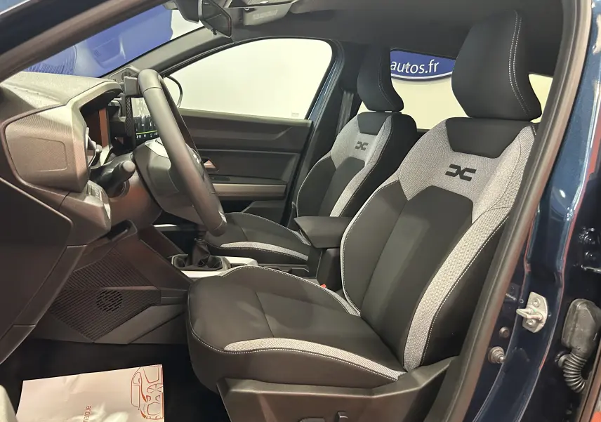 Vue intérieure côté conducteur du Dacia Bigster bleu indigo, mettant en valeur les sièges bi-ton tissu avec logo brodé.