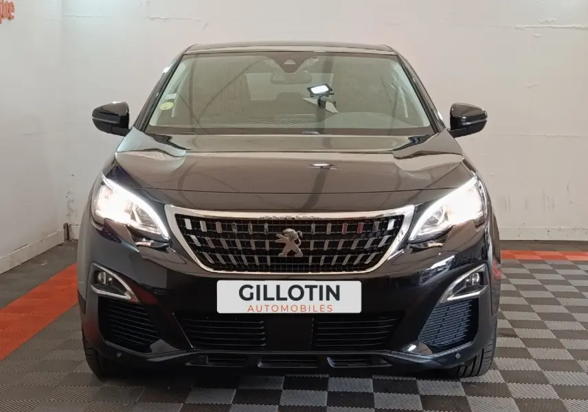 Vue frontale d’un Peugeot 5008 noir 2020 avec phares allumés et calandre chromée, en intérieur showroom.