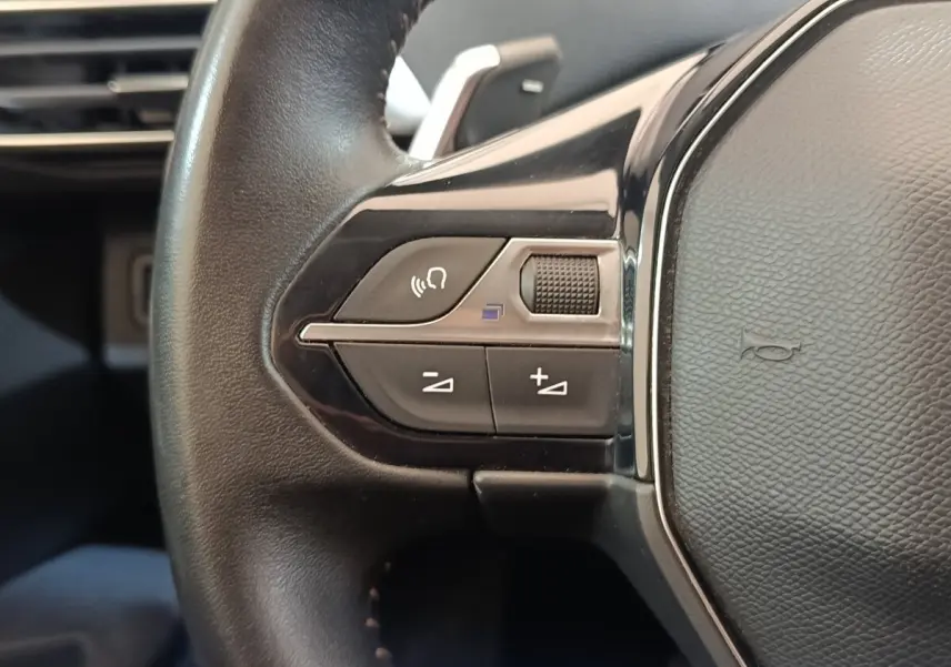 Gros plan sur les commandes gauche du volant cuir noir du Peugeot 5008, avec boutons de volume et reconnaissance vocale.