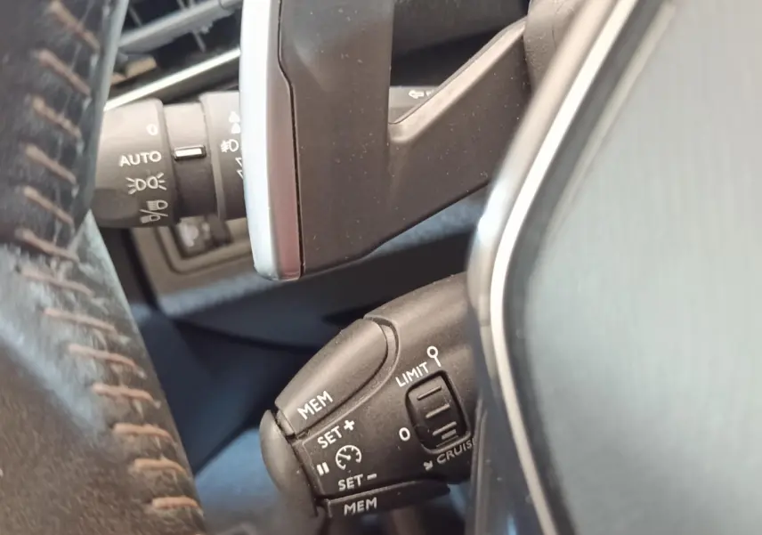 Gros plan sur la commande de régulateur de vitesse noire, vue côté gauche du volant cuir d’un Peugeot 5008 noir.