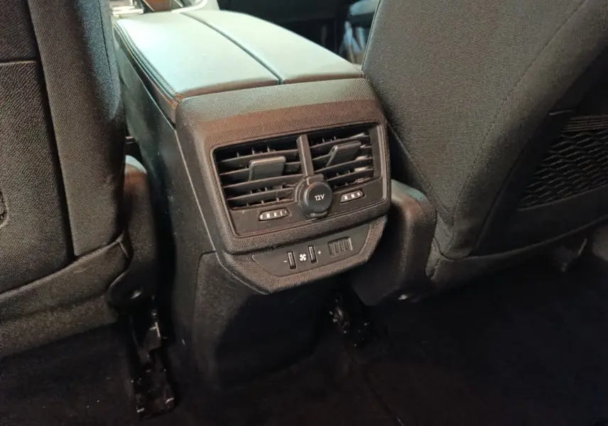 Vue rapprochée des commandes de ventilation arrière et prise 12V entre les sièges noirs du Peugeot 5008 2020.