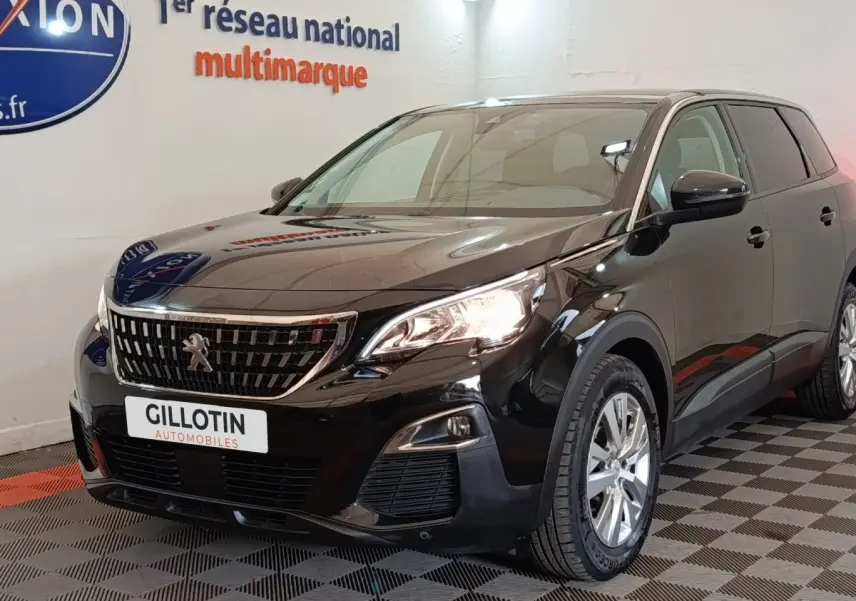 Peugeot 5008 noir vue 3/4 avant droit, avec calandre chromée et phares allumés en intérieur showroom.