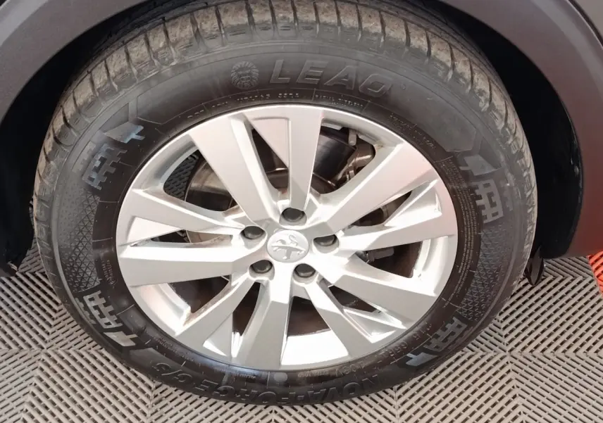 Gros plan sur la roue avant droite d’un Peugeot 5008 noir, avec jante alliage argentée et pneu LEAO.