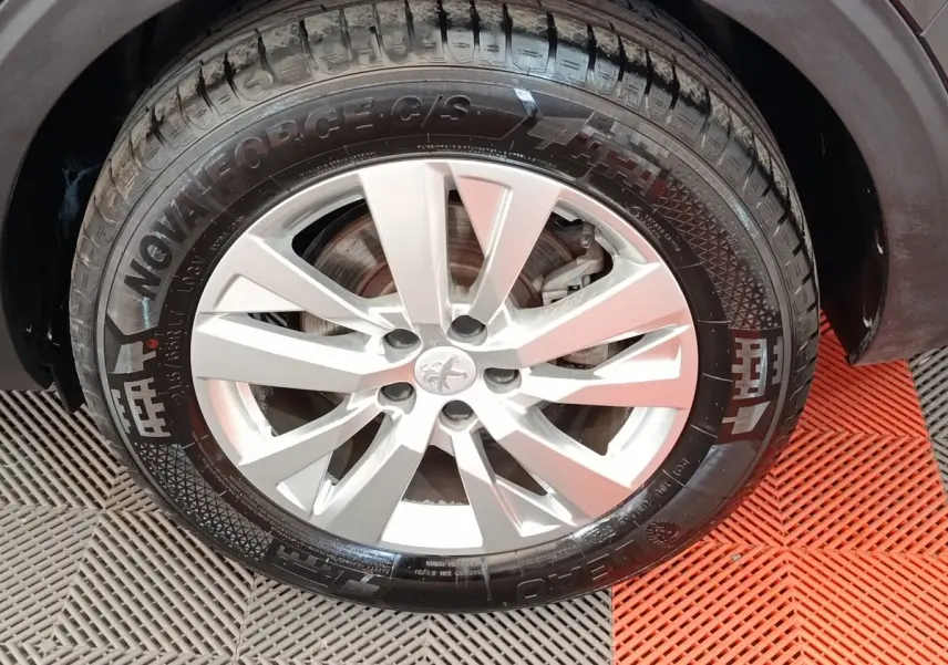 Gros plan sur la roue avant droite d’un Peugeot 5008 noir, jante alliage argentée à 5 doubles branches.