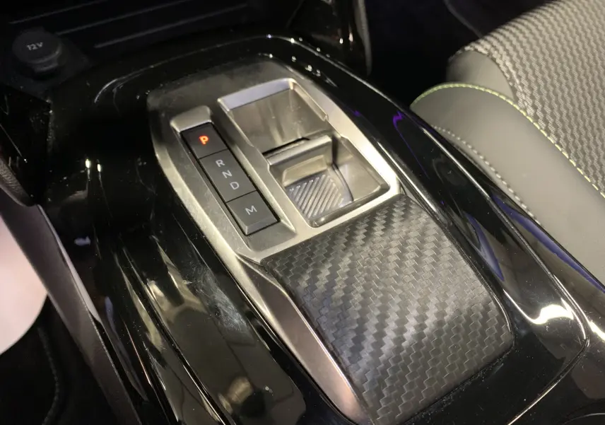 Gros plan sur la console centrale noire brillante avec levier de vitesses électronique et insert effet carbone dans un Peugeot 2008 2023.