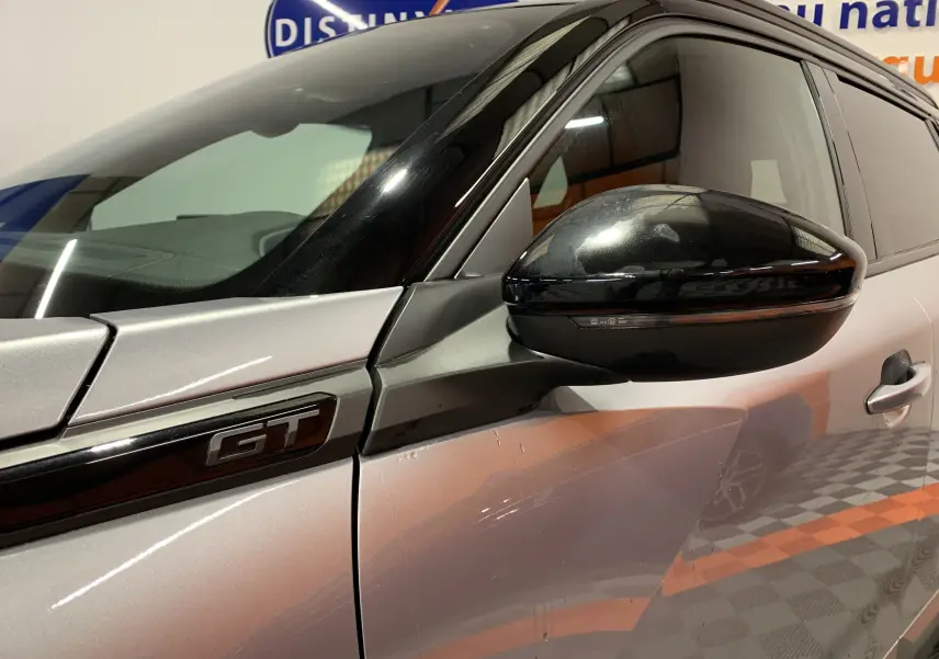 Gros plan sur la porte côté gauche d’un Peugeot 2008 gris 2023 avec badge GT et rétroviseur noir brillant.