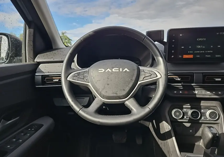 Vue frontale du volant noir DACIA Jogger 2024 avec tableau de bord et écran tactile central allumé.