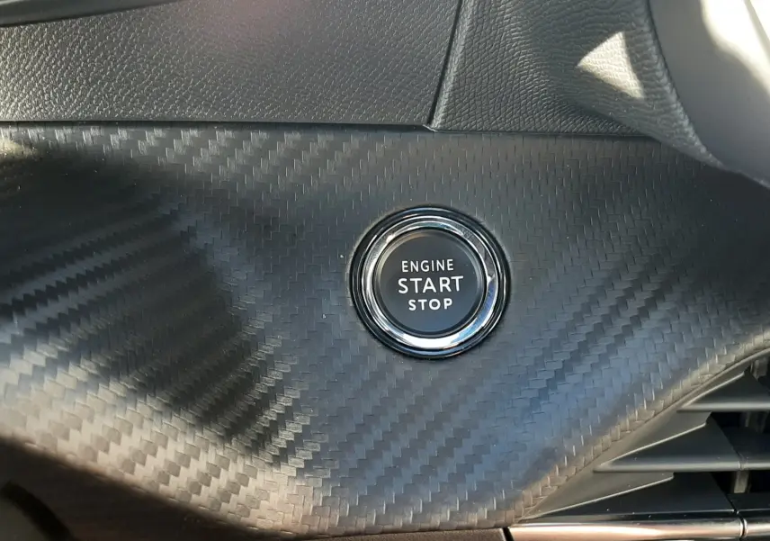 Bouton démarrage moteur circulaire sur tableau de bord effet carbone noir du Peugeot 2008 hybride 2025.