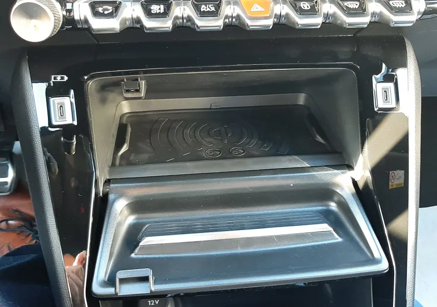 Vue rapprochée de la console centrale du Peugeot 2008 1.2 Hybrid 145ch GT avec boutons de commande et plateau de recharge sans fil.