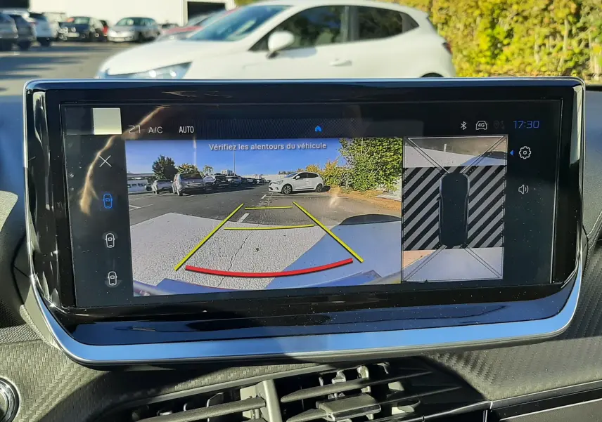 Écran intérieur affichant la caméra de recul avec vue 3/4 arrière droite d'un Peugeot 2008 gris selenium en extérieur.