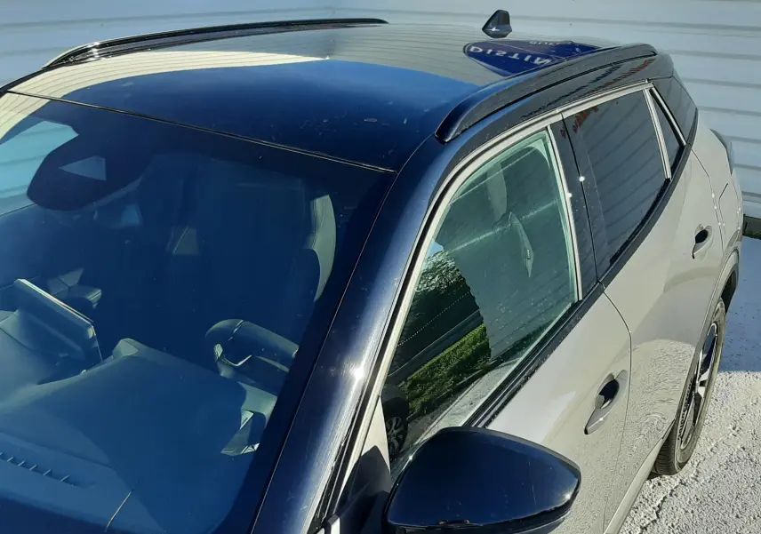 Vue plongeante sur le côté gauche d'un Peugeot 2008 gris selenium avec toit noir brillant et rétroviseur assorti.