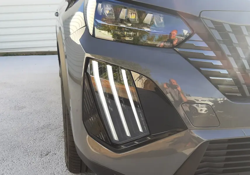 Gros plan sur le phare avant gauche et la calandre du Peugeot 2008 gris selenium, mettant en valeur ses lignes LED verticales distinctives.