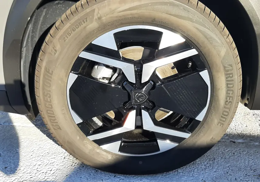Gros plan sur la roue avant droite d'un Peugeot 2008 gris selenium, jante alliage noire et argentée au design moderne.