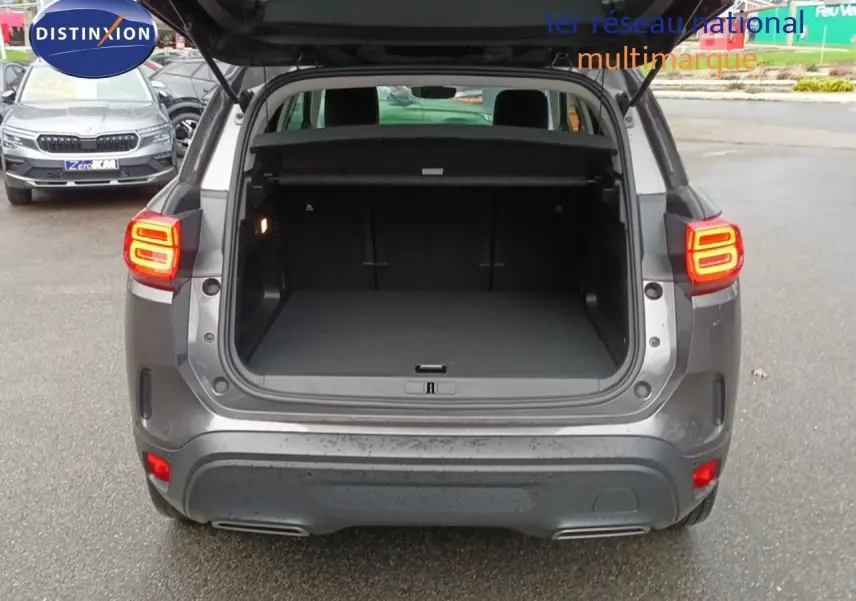 Vue arrière d'un Citroën C5 Aircross hybride rechargeable gris platinium avec coffre ouvert et feux arrière allumés.